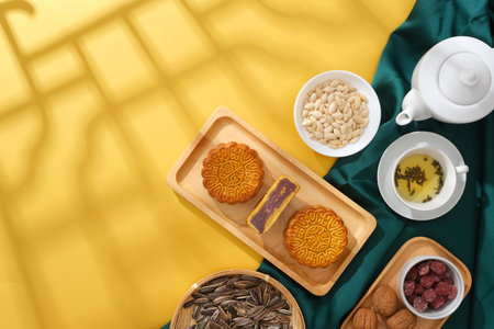 Minimalist style tea party table with mooncakes decorated with set of tea, nuts and jams on green silk cloth on a yellow background. Blank space for display product, design or copy spaceの写真素材