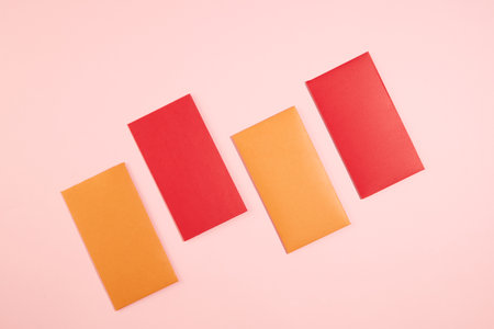 Two orange lucky money envelopes and two red lucky money envelopes are arranged alternately on a pink background. Lucky envelopes are wishes for good luck, health, peace, and fortune to everyone.の写真素材