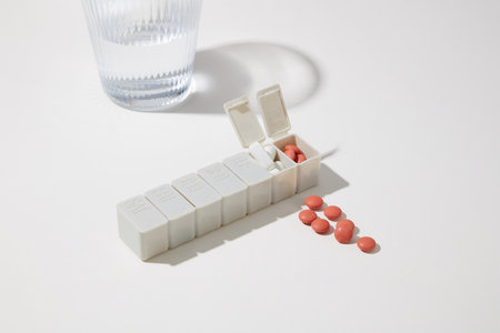Close-up of a daily pill box with tablets and a glass of water on a minimalist white background. Medical space for drug advertising. Medical concept.の写真素材