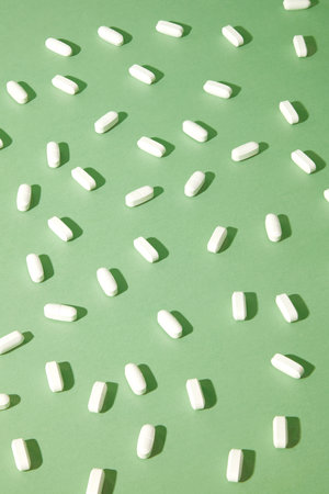 View from above of white pills are densely arranged on a pastel green background. Medicine background for advertising. Minimalist space. Medical topic.の写真素材