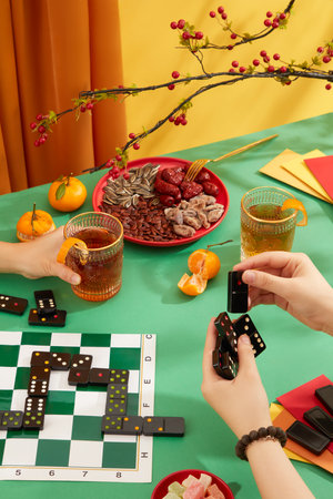 Two people were playing dominoes on the table, surrounded by a plate of dried nuts and jam, tangerines, two glasses of carbonated water and red envelopes. The Tet atmosphere is bustling.の写真素材