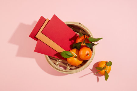 View from above of tangerines and lucky money envelopes are inside a bamboo steamer on a pink background. Tet theme for advertising and design.の写真素材