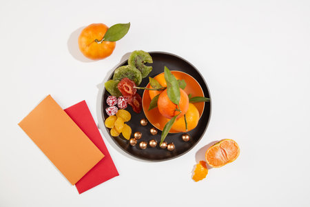 Top view of jam and tangerines on a black tray, two lucky money envelopes on a white background. Simulate the Tet tea table. Images for advertising.の写真素材