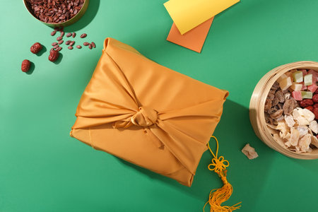 Top view of a gift box wrapped in yellow silk, a tray of jam and melon seeds, and lucky money...