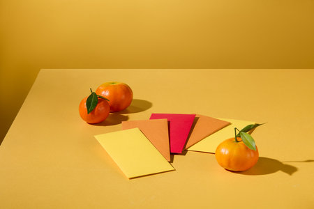 Close up of lucky money envelopes displayed on a yellow background with tangerines. Space for display and design. New Year theme. Advertising scene.の写真素材