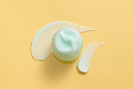 Looking from above, a jar of dense-textured moisturizer in a light blue against a yellow background....