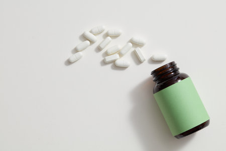 An unlabeled medicine bottle with scattered pills on a white background. Medication for body healing. Mockup for pharmaceutical advertising.の写真素材