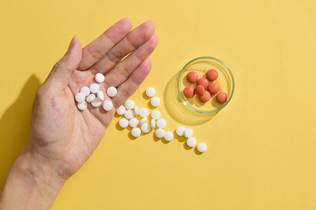 In the palm of the hand lie some pills, while others are scattered around, adorned with a petri dish...