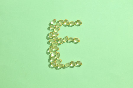 Vitamin E capsules arranged in the shape of the letter E on a light green background. Vitamin E promotes smooth, youthful skin, reducing wrinkles. Copy space for advertising functional foods.の写真素材