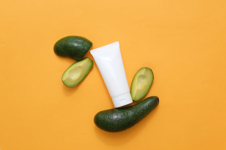 Against the yellow background, an empty plastic tube decorated with fresh slices of avocado slices. Mockup packaging, cosmetics design. Minimalist concept for advertising with organic ingredientの写真素材