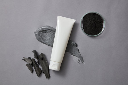A tube without label is decorated with a smear of clay mask and a petri dish of activated charcoal powder. Activated bamboo charcoal can improve dry or oily skin, or heal acneの写真素材