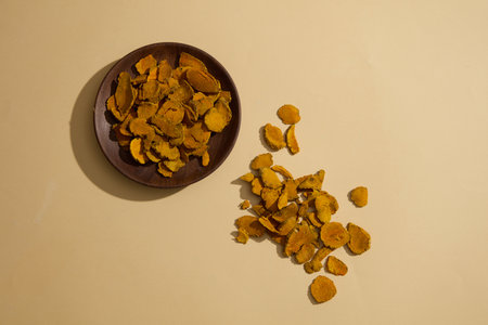 A dish of dried turmeric slices displayed on beige surface. Dried Turmeric (Curcuma longa) is one of...