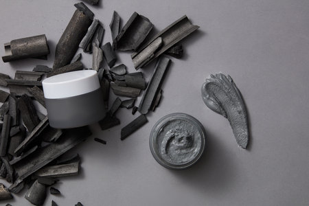 A smear of clay mask texture displayed with cosmetic jars and a pile of activated charcoal sticks....