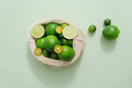 View from above of many kumquat and lime contained inside a mesh bag. Pastel background. Lime and Kumquat juice may promote weight lossの写真素材