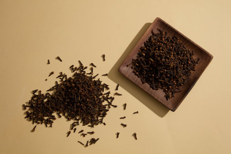 Piles of Cloves placed on beige surface and on square-shaped dish. Cloves (Syzygium aromaticum)...