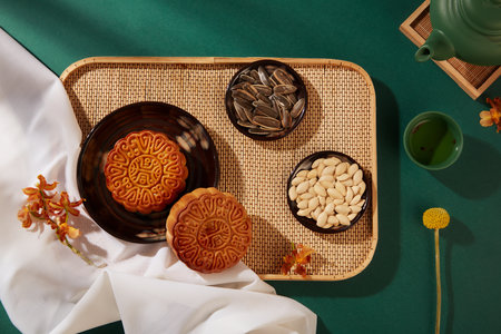 Bamboo tray with mooncakes and dishes of pumpkin seeds and sunflower seeds arranged on. Green background. Mid-Autumn Festival Food Advertisingの写真素材