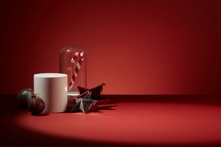 White podium in cylinder-shaped decorated with baubles, two stars and a glass cage with candy cane inside. Vacant space in the right side for product promotionの写真素材
