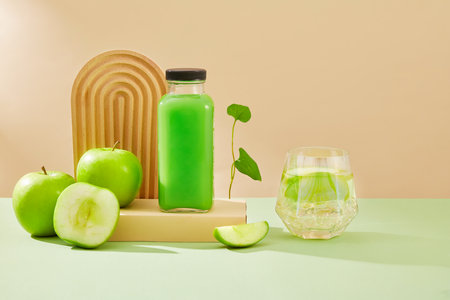 Beige podium with a glass bottle of green apple juice standing on. A beautiful glass displayed. Green Apple (Malus domestica) can manage blood pressure levels and blood sugar levelsの写真素材