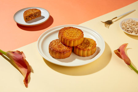 Some traditional mooncakes stacked on each others on white plate. A dish containing pumpkin seeds...