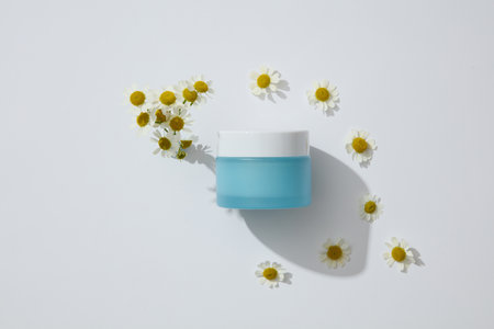 Blue jar without label arranged with white flowers. Chamomilla (Matricaria chamomilla) is a great ingredient in topical treatments for dark spots on the skinの写真素材