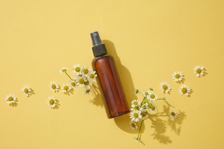 Against yellow background, some flowers and a pump bottle are featured. Top view. Branding mockup with Chamomilla (Matricaria chamomilla) extractの写真素材