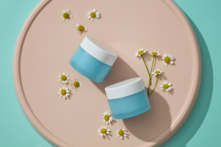 Unbranded blue jars placed on pink dish with fresh flowers. Chamomilla (Matricaria chamomilla) extract can be used to treat a variety of cosmeticの写真素材