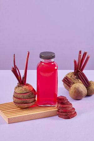 Unlabeled glass bottle of pink juice decorated with stacks of many beetroot round slices. Purple background. Branding mockup with empty label bottleの写真素材