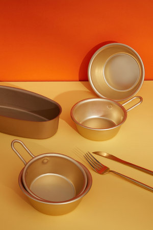 Against the color background, set of golden pots and trays made of stainless steel decorated with knife and fork. Pop art design.の写真素材