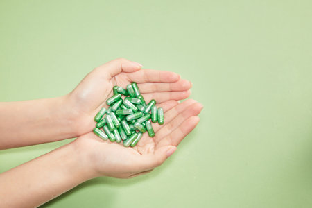 A lot of vitamin capsules are placed in the palm of a woman's hands on a green background. Blank...