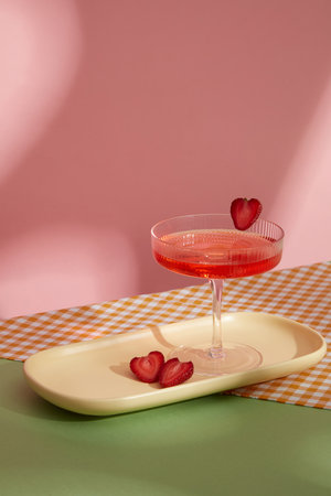 Minimal concept for advertising and branding drink. Front view of glass juice with some strawberry slices on rectangle plate decorated with checkered scarf on pink background with window shadowの写真素材