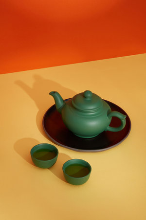 A ceramic set of teapot decorated on color paper. A green pot placed on round black place. Blank minimal scene with copy space for advertising and branding product.の写真素材