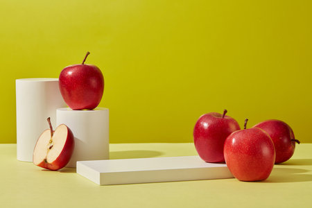 Front view of cylinder white podiums and some ripe red apples decorated on a green background. Blank space to place your design. Scene for advertising and branding cosmetic product with appleの写真素材