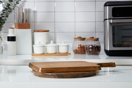 Stacked of wooden cutting board form an empty podium for display product. In the background is the counter with spice boxes, knife tray and microwave decorated on white tile backgroundの写真素材