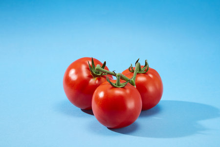 Front view of three juicy red ripe tomatoes (Solanum lycopersicum) with green stems on a blue background. Tomatoes have a lot of nutrients that are good for healthの写真素材