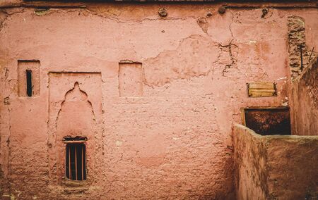 Worn and dirty pink ochre painted adobe wall, in the medina of Marrakech, with windows with arabesque motifsの写真素材
