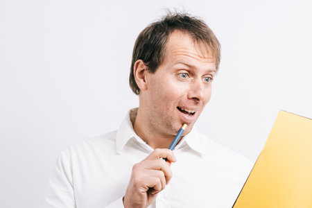 Young man looking at a yellow folder drinking coffee in a blues cup. White background.