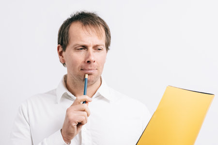 Young man looking at a yellow folder drinking coffee in a blues cup. White background.の写真素材
