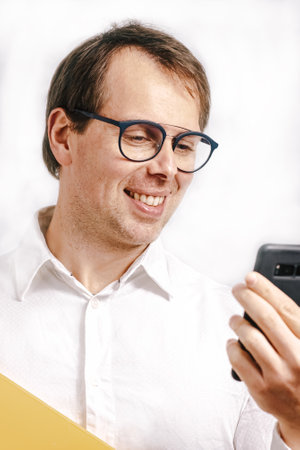 Young man looking at a yellow folder drinking coffee in a blues cup. White background.の写真素材