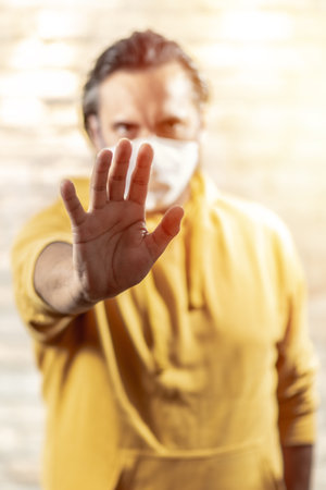 Close up of man with mask showing smartphone wearing yellow hooded .. Shining light.の写真素材