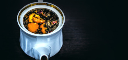White porcelain brewer or kettle with a golden border without a lid on a dark background. Brewed tea with orange and flowersの写真素材