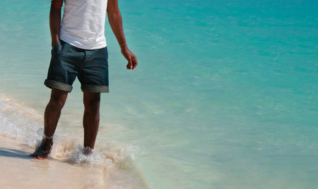 A black man in the water with a cigarette on the shore of the Indian Ocean. White T-shirt, denim shorts and tan. Zanzibar of Tanzaniaの写真素材