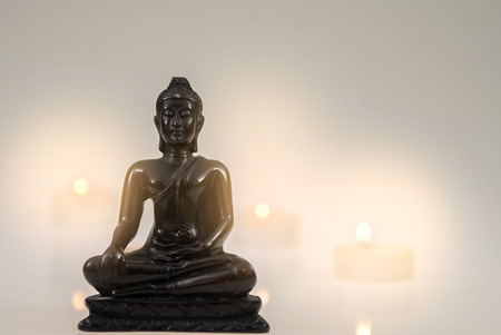 Little Buddha figure with candle lights behind and white and grey gradient background. High res photo taken with a full frame dslr.の写真素材