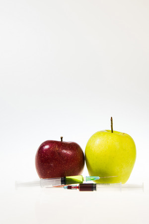 Two syringes with chemicals next to the two apples. White and grey gradient background. High res photo taken with a full frame Nikon D610.の写真素材