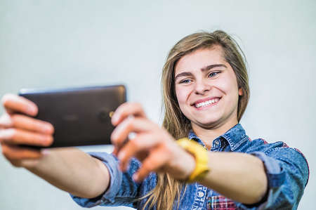 Teenager girl is taking a photo of herself. White background.の写真素材