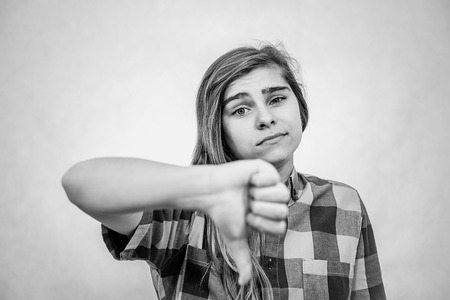 Young teenage girl is showing thumbs down symbol. She looks disappointed.の写真素材