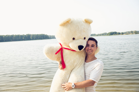 Handsome young man is fooling around with his massive teddy bear.の写真素材