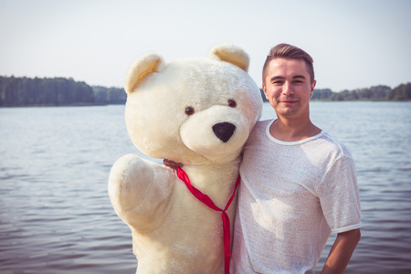 Handsome young man is fooling around with his massive teddy bear.の写真素材