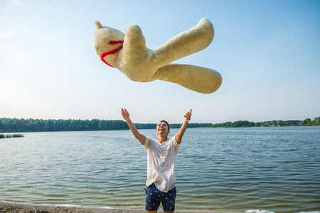 Handsome young man is fooling around with his massive teddy bear.の写真素材