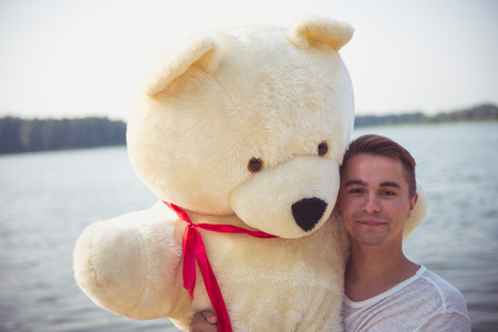 Handsome young man is fooling around with his massive teddy bear.の写真素材