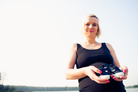 Portrait of a young and beautiful pregnant woman holding little shoes of her future child.